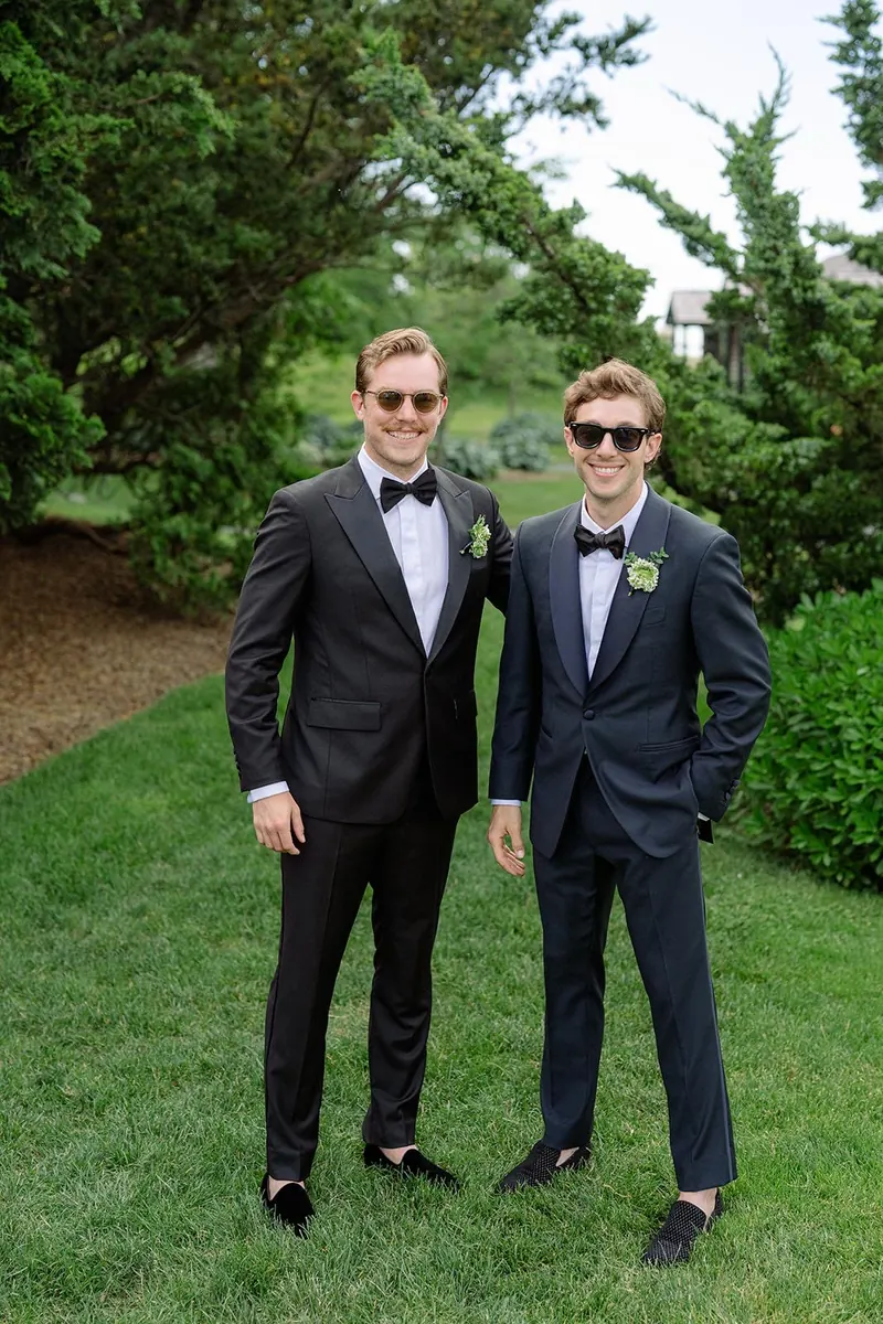 Groom and best man in bespoke black tuxedos in a garden