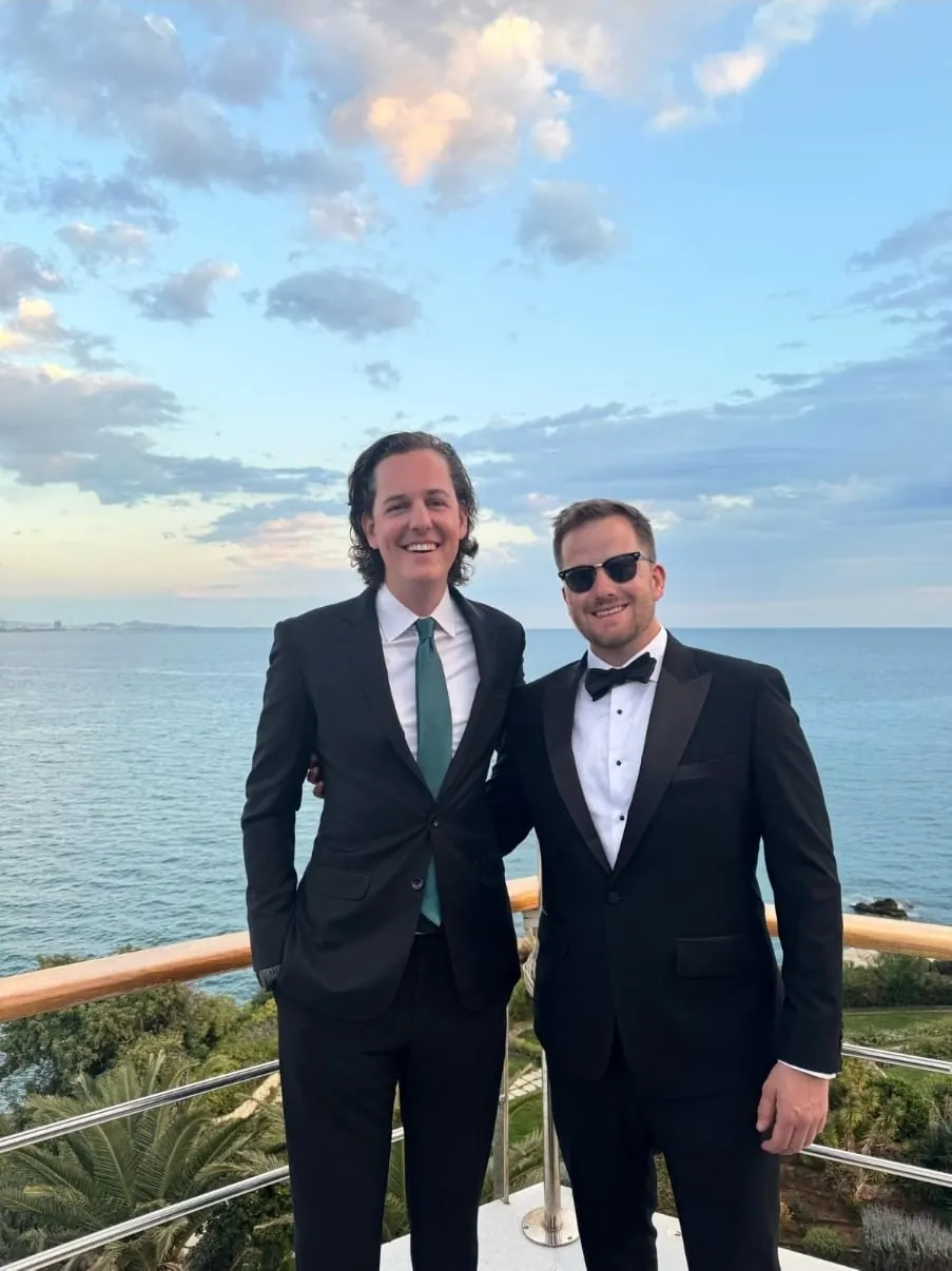 Two clients in a bespoke black suit and tuxedo by the sea
